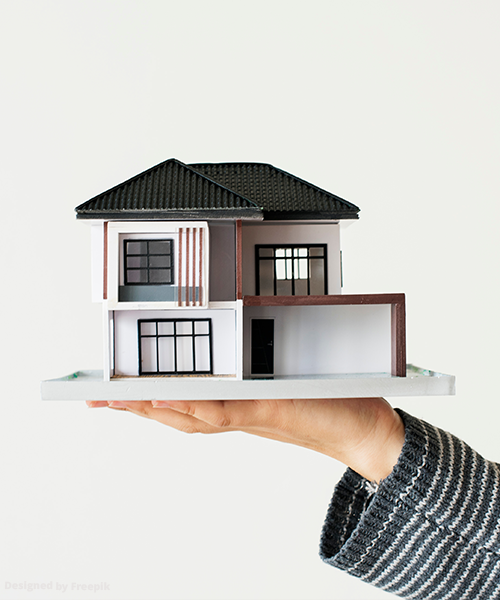 Model domu jednorodzinnego stojący na wyciągniętej ręce.